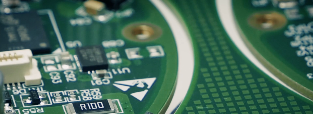 Close-up of a green printed circuit board (PCB) featuring various electronic components, including resistors and a microchip, with labels and symbols.